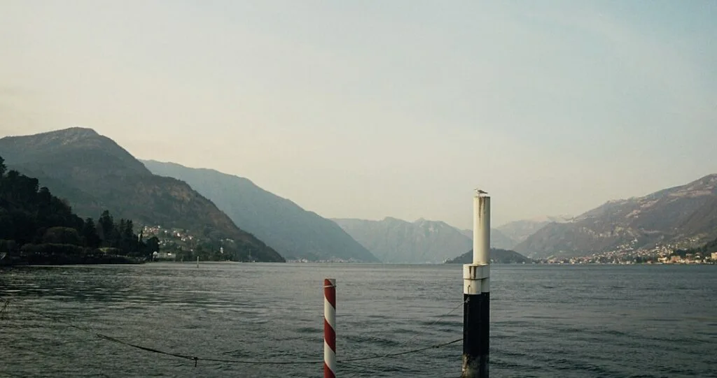 Pfahl im Wasser vor Lac come, entfernte Bergkulisse sichtbar