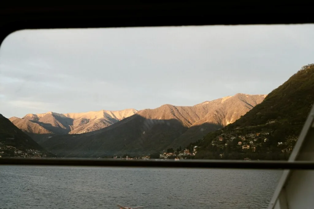Blick durch Schiffsfenster auf Lac come, Berge im Abendlicht