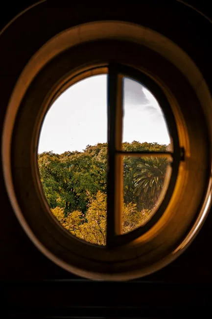 Rundes Holzfenster mit Aussicht auf grüne Bäume und Palmen