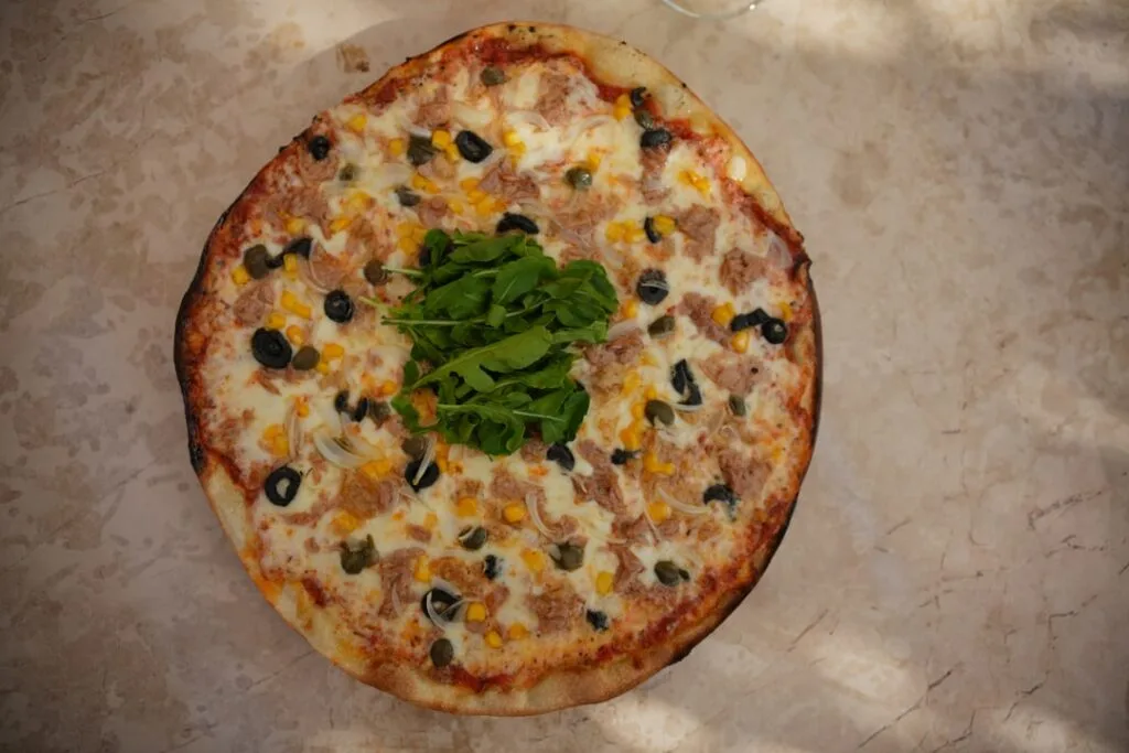 Pizza mit Rucola, Oliven und Thunfisch auf dem Tisch am Comer See