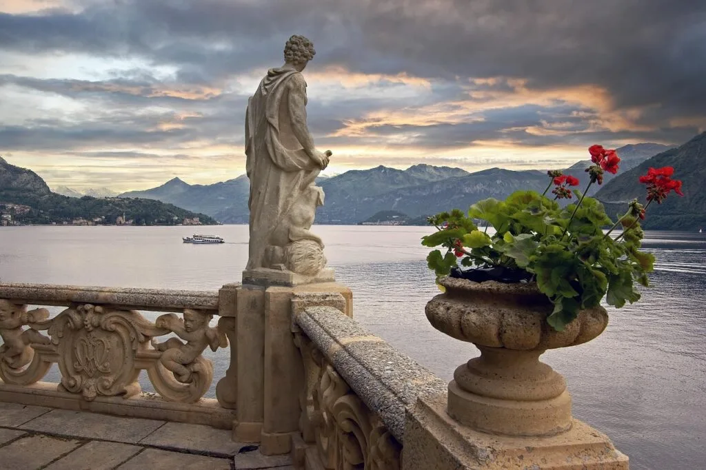 Balustrade sculptée avec statue et géraniums rouges face au Lac de Côme