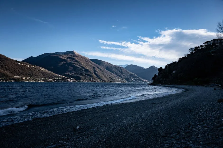 Kieselstrand am Comer See bei Dämmerung, bergige Uferlinie sichtbar