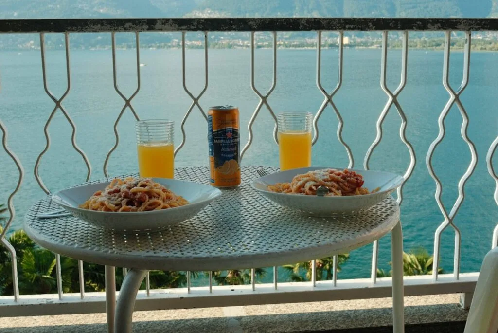 Balkontisch mit zwei Tellern Pasta und Blick auf den Comer See