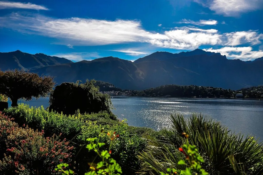 Ufer und Gärten mit glitzernden Spiegelungen des Comer Sees und Bergen