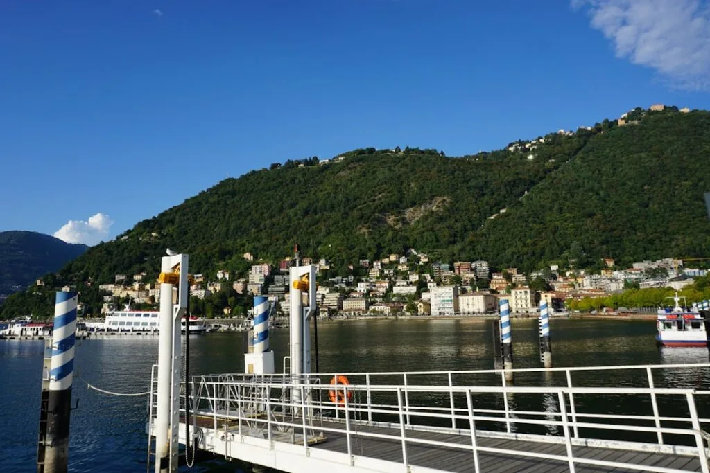 Fähranleger mit blau-weiß gestreiften Pfählen und Stadt am Lac come