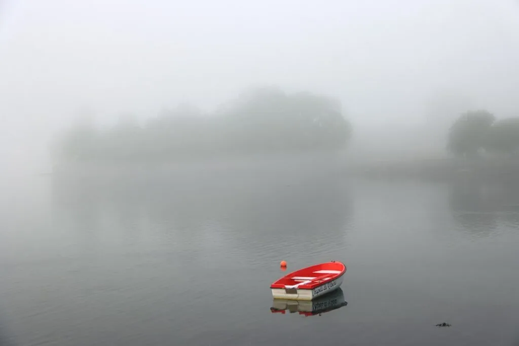 Kleines rotes Boot, das im Nebel auf dem Comer See schwimmt