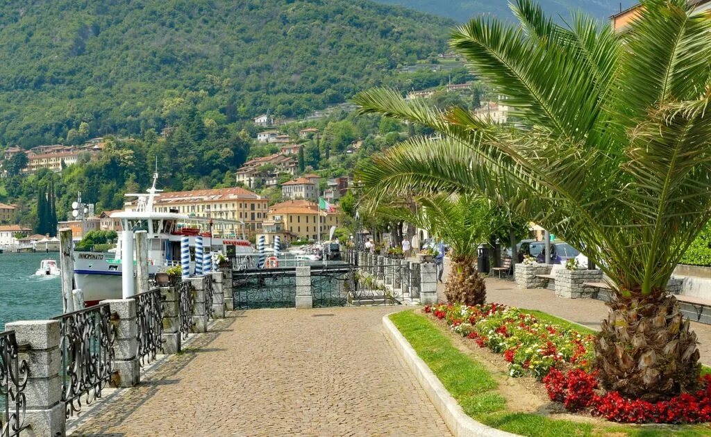 Uferpromenade in Menaggio mit Palmen, Blumenbeeten und einem angelegten Fährschiff