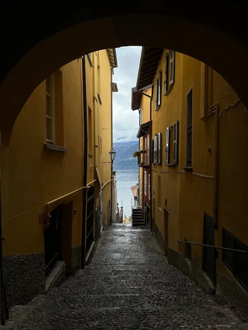 Ruelle pavée encadrée par arcades jaunes, ouverture sur le Lac de Côme